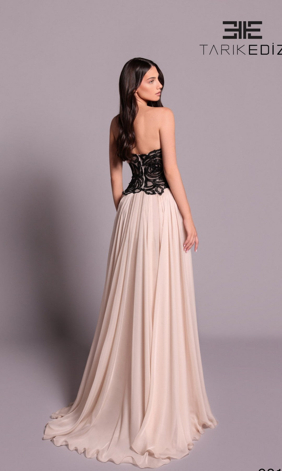 A woman models the Tarik Ediz 99101 long formal dress, featuring a chiffon A-line silhouette with a lace fitted bodice and flowing cream skirt, as she stands facing away from the camera against a plain background.